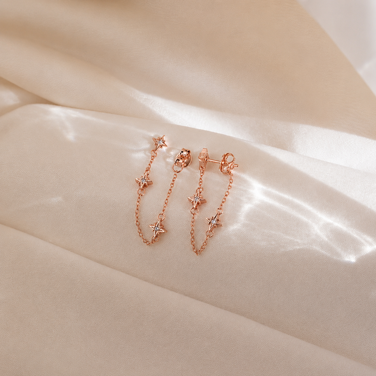 Rose gold chain earrings with star details on a beige fabric background