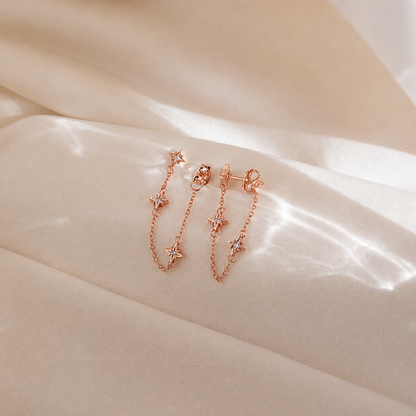Rose gold chain earrings with star details on a beige fabric background