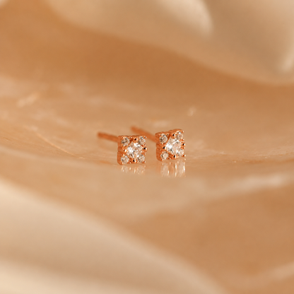 Rose gold earrings with small diamonds on a beige fabric background