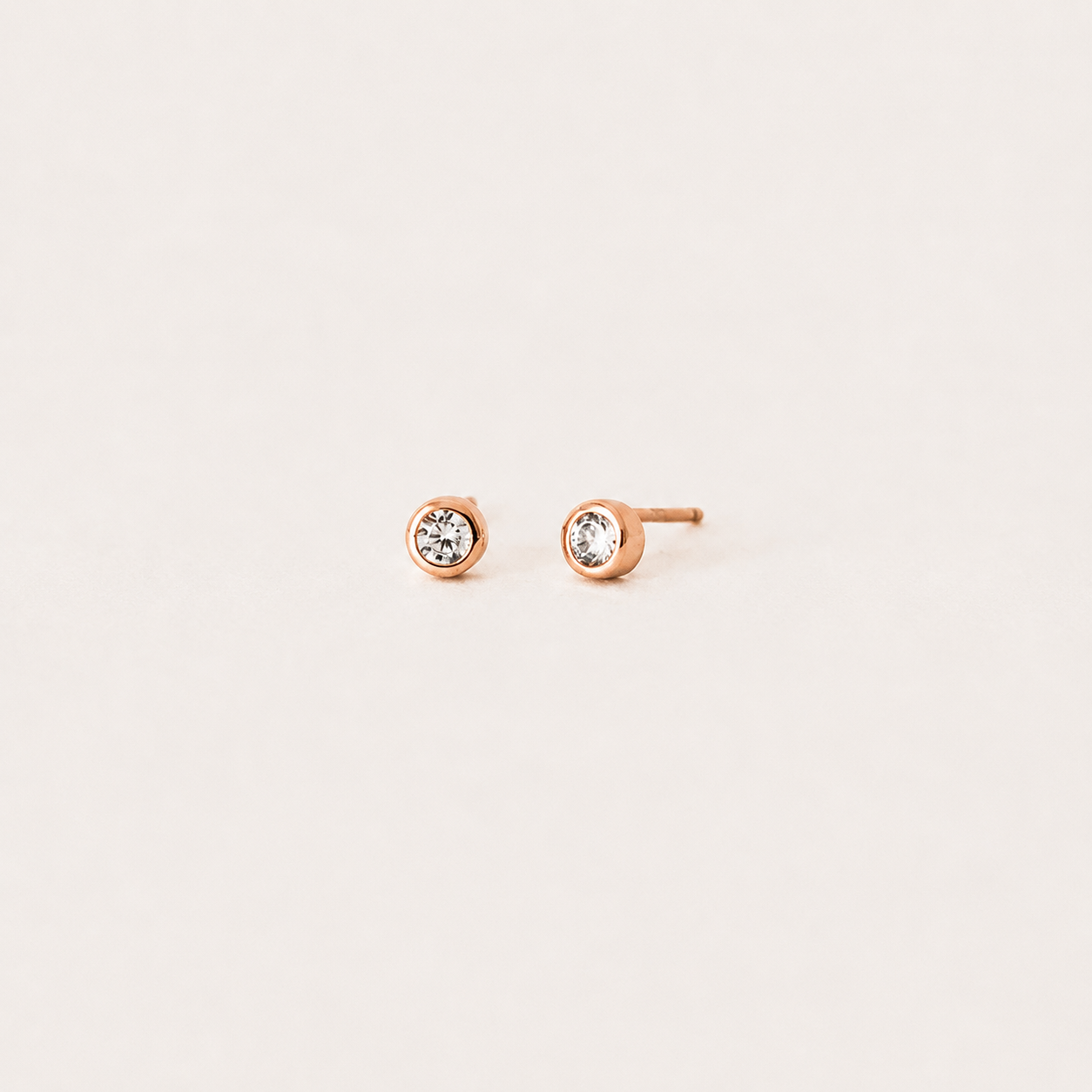 Rose gold stud earrings with clear gemstones on a light beige background