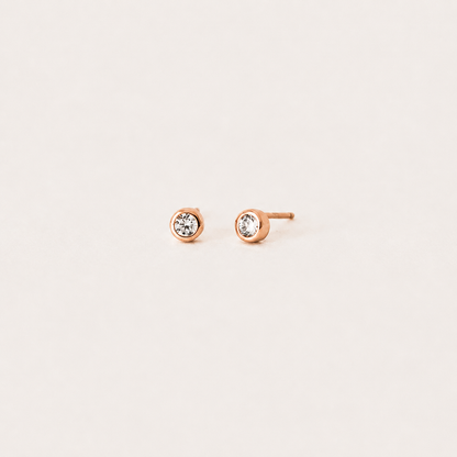 Rose gold stud earrings with clear gemstones on a light beige background