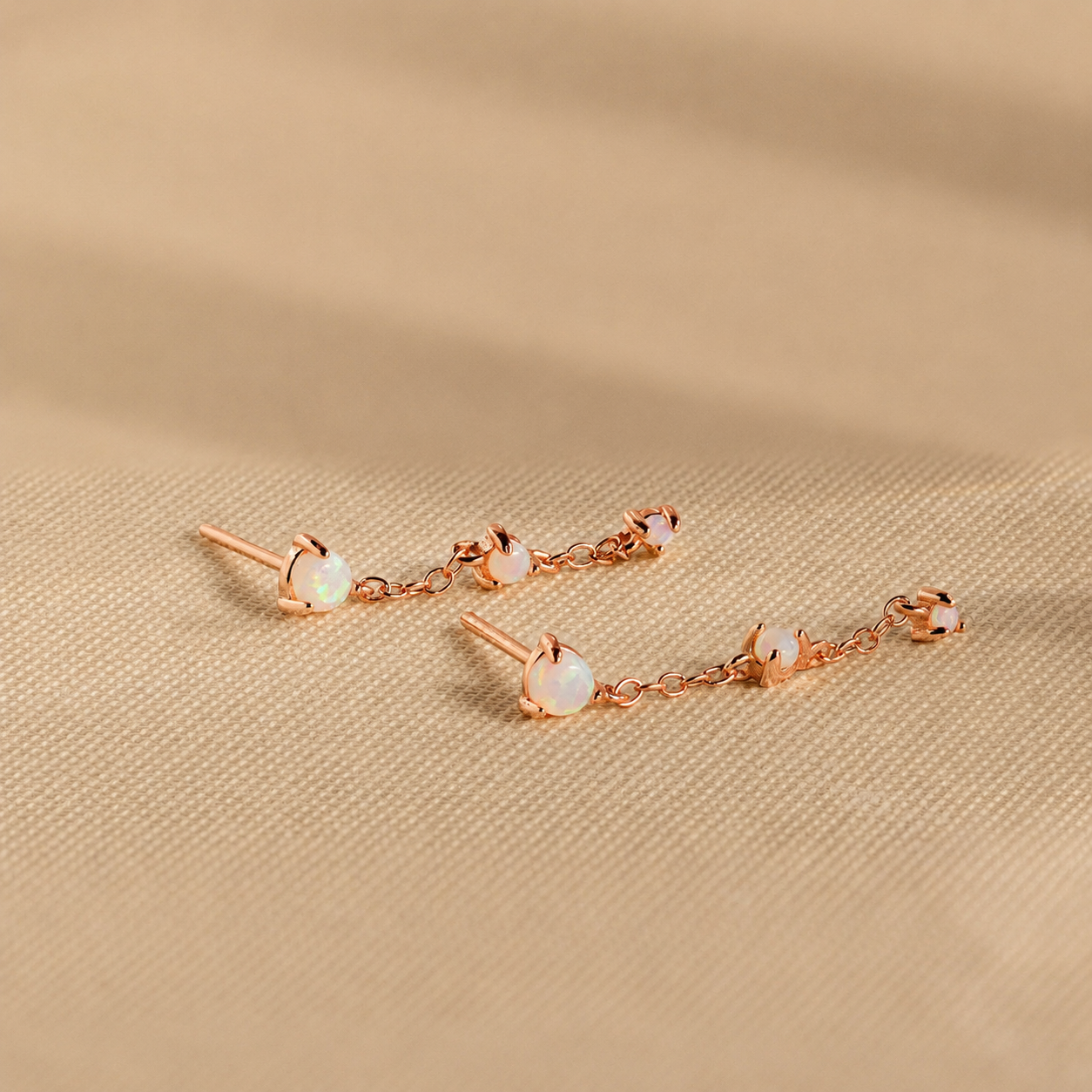 Rose gold earrings with opal stones on a beige fabric background