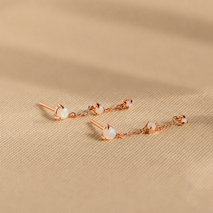 Rose gold earrings with opal stones on a beige fabric background