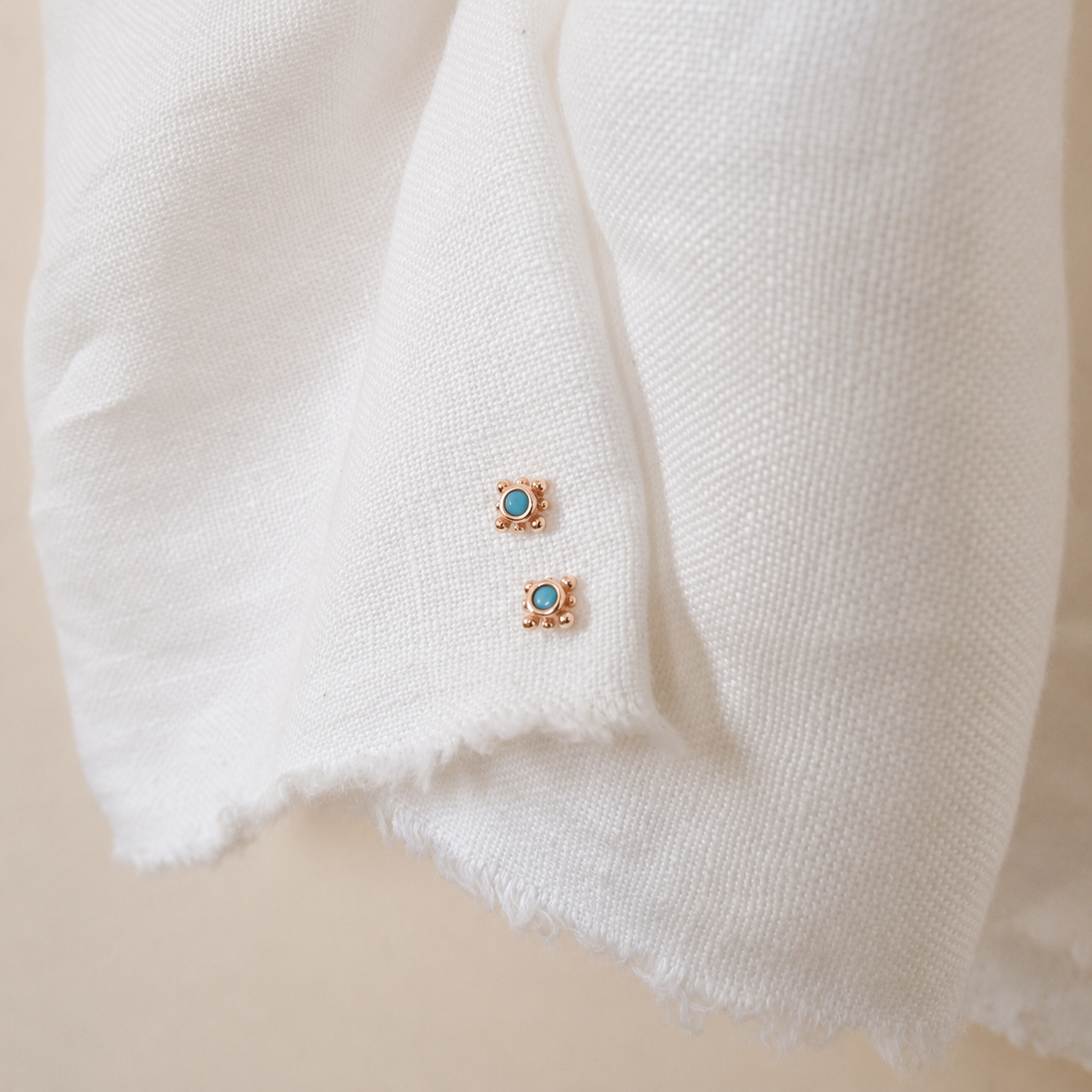 Pair of gold earrings with turquoise stones on a white fabric background