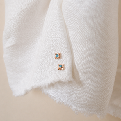 Pair of gold earrings with turquoise stones on a white fabric background