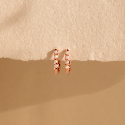 Rose gold hoop earrings with embedded stones on a beige background
