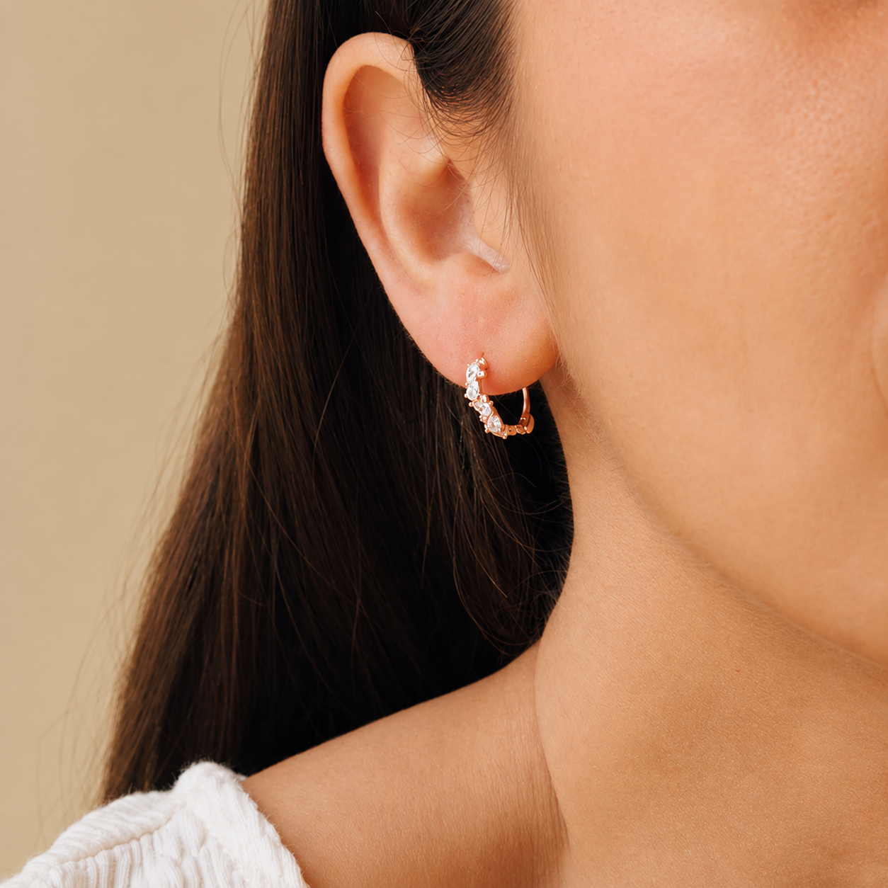 Close-up of a person wearing a gold hoop earring with small stones against a beige background
