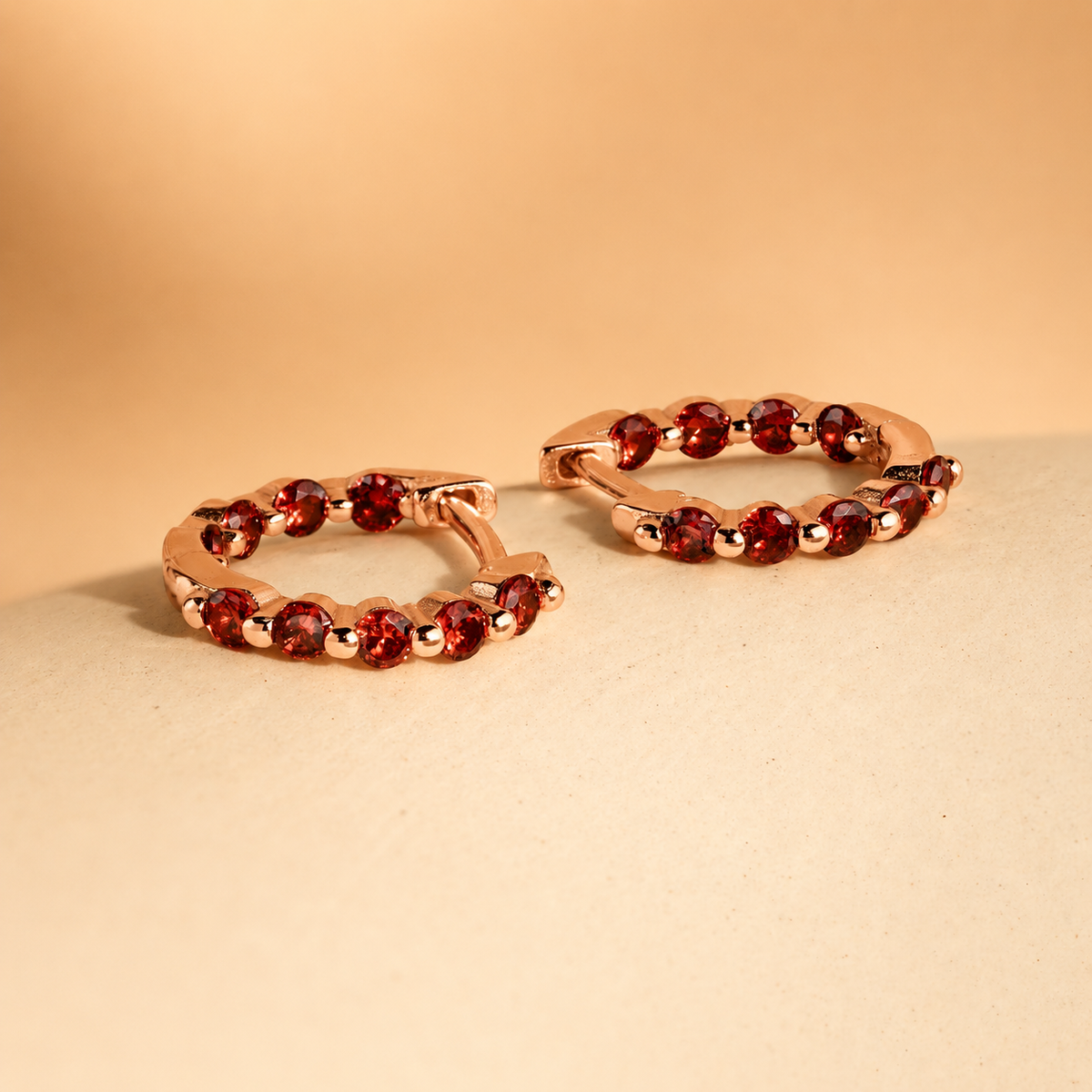 Pair of hoop earrings with red gemstones on a beige background