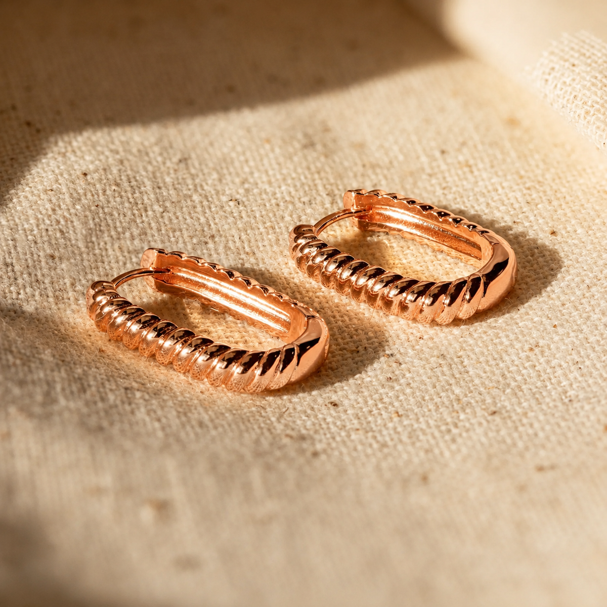 Rose gold hoop earrings on a textured beige fabric background