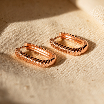 Rose gold hoop earrings on a textured beige fabric background