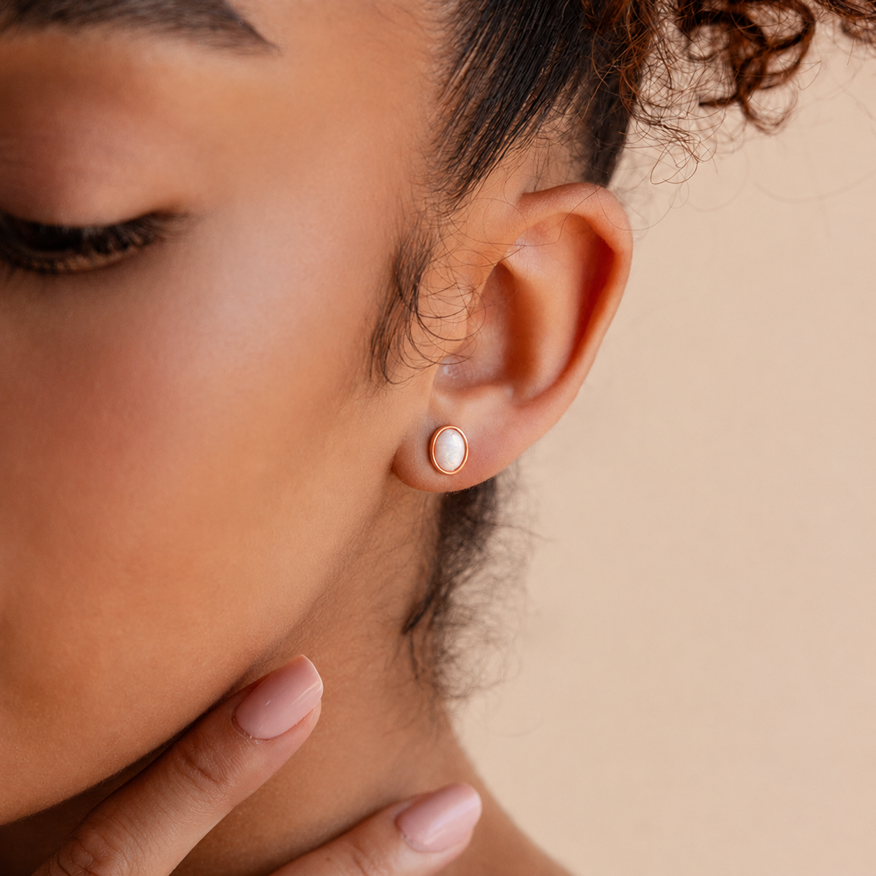 Close-up of a woman wearing a rose gold earring with a pearl-like stone on a beige background