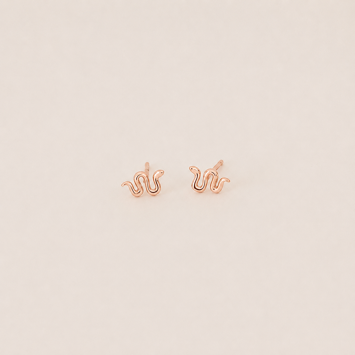 Rose gold squiggle-shaped earrings on a light beige background