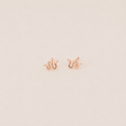 Rose gold squiggle-shaped earrings on a light beige background