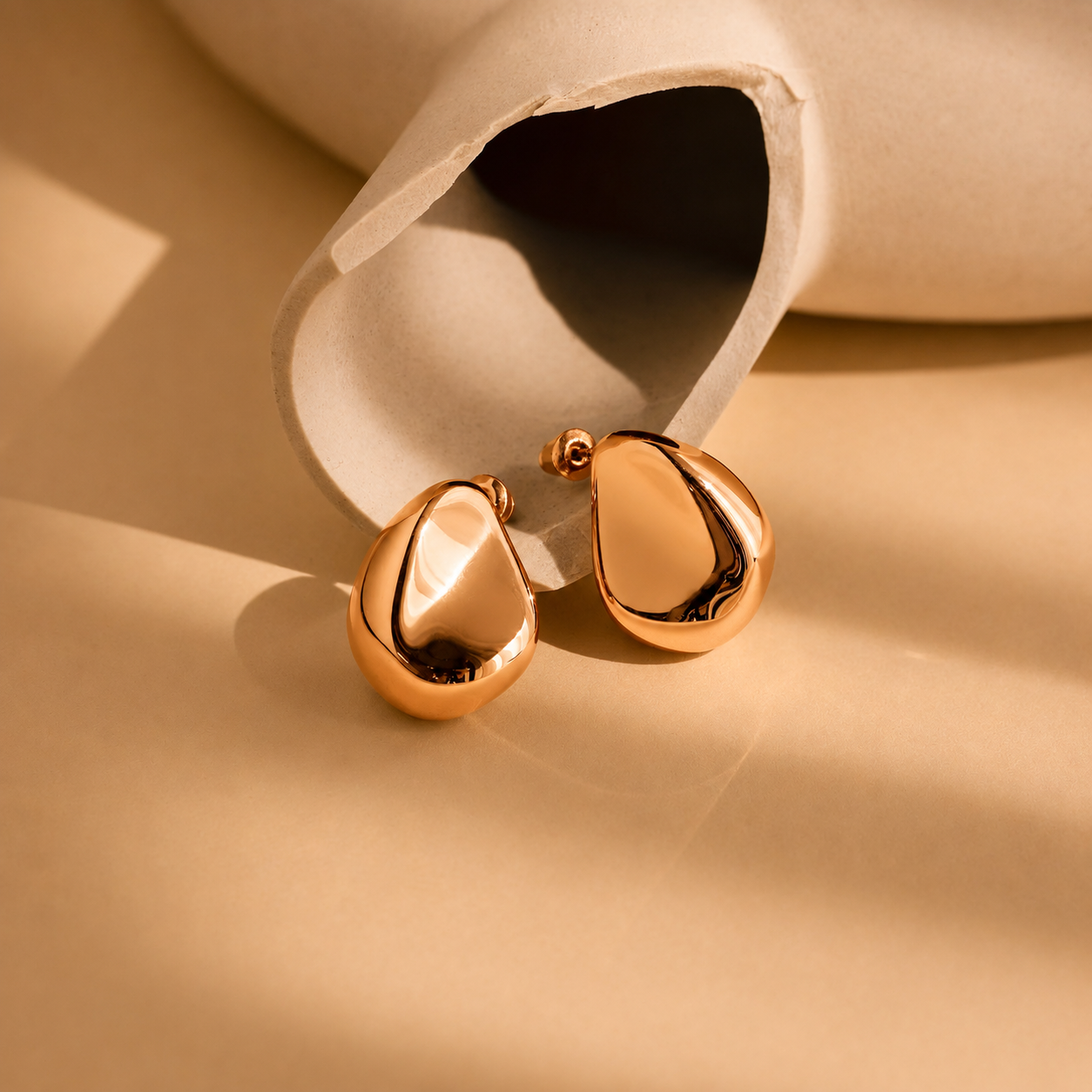 Gold teardrop earrings on a beige background