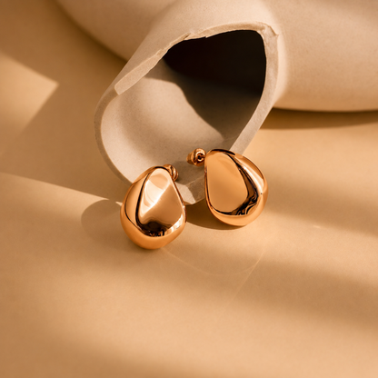 Gold teardrop earrings on a beige background