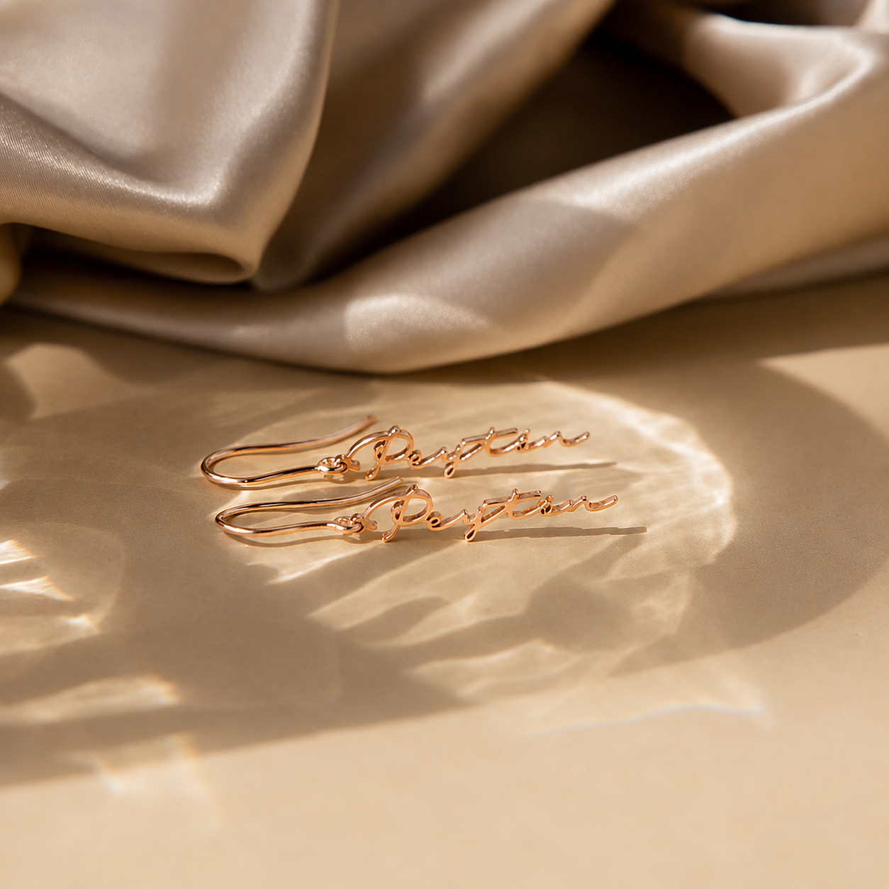 Gold earrings with 'Perfection' engraving on a beige fabric background