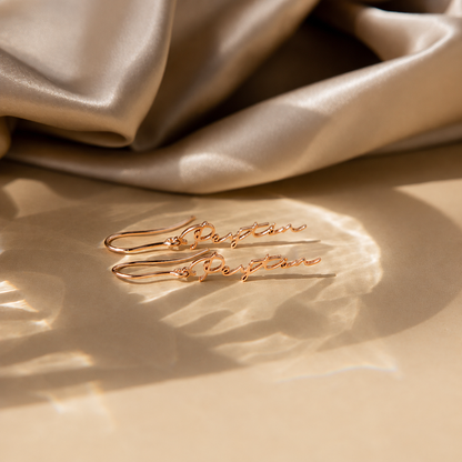 Gold earrings with 'Perfection' engraving on a beige fabric background