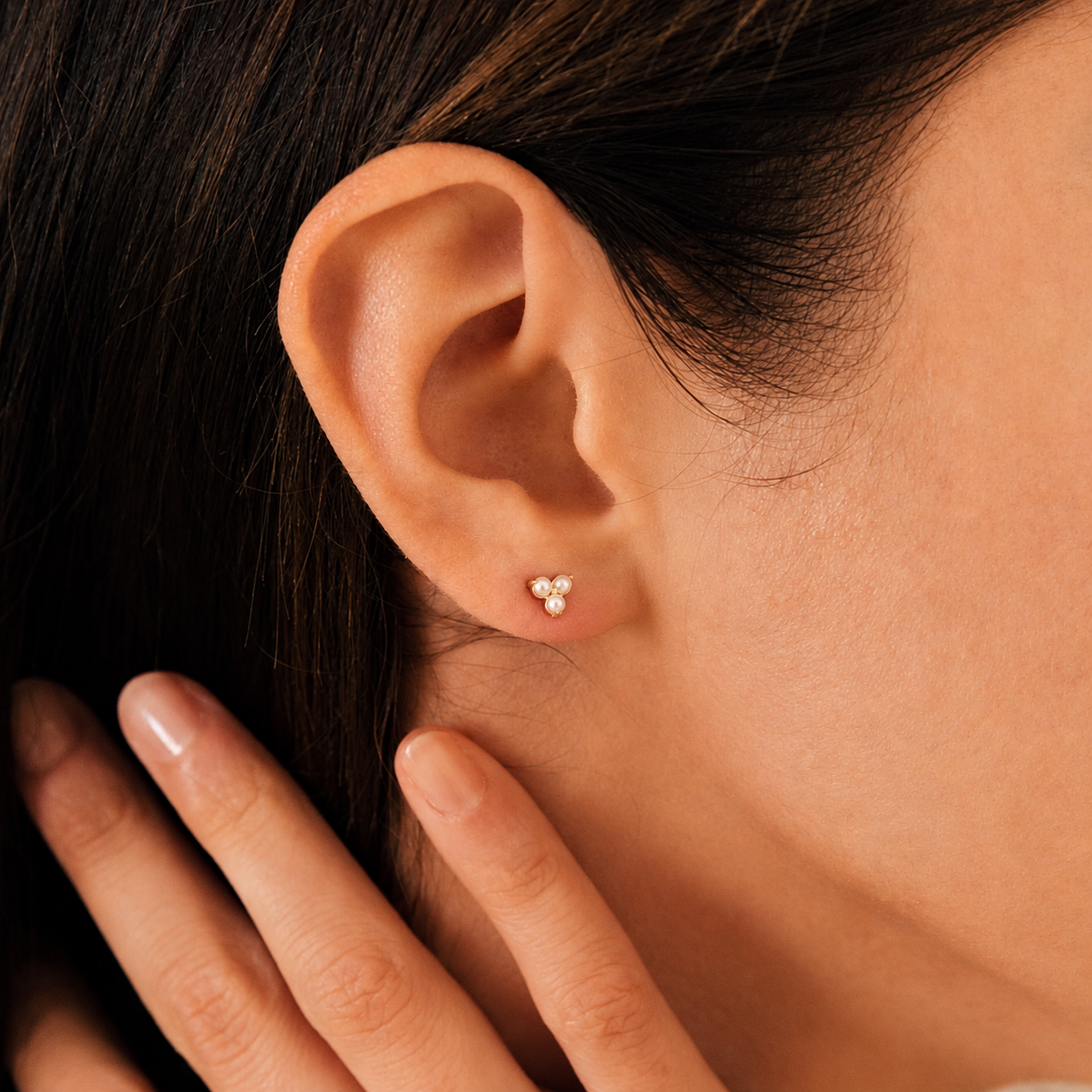 Close-up of an ear wearing a gold earring with a hand touching the hair.
