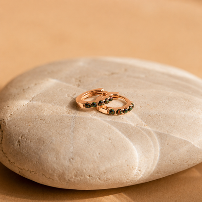 Rose gold hoop earrings with green gemstones on a beige stone