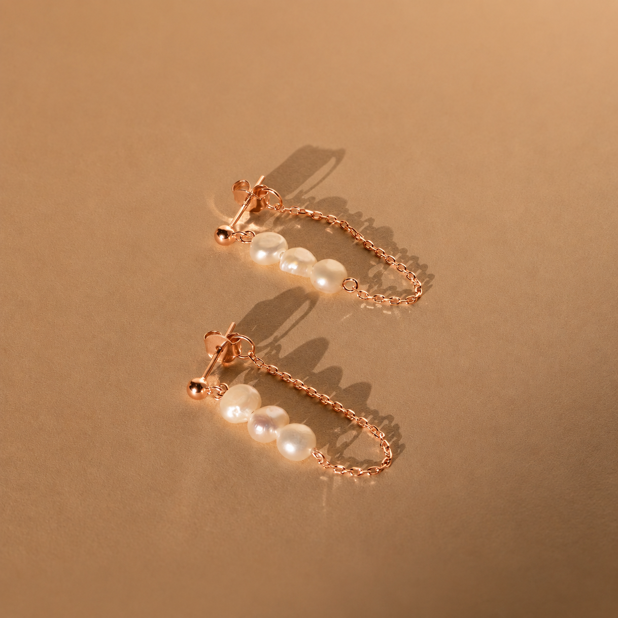 Rose gold earrings with pearl-like beads on a beige background