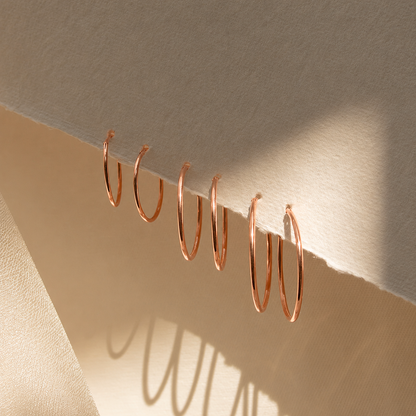 Set of rose gold hoop earrings on a beige surface with soft shadows.