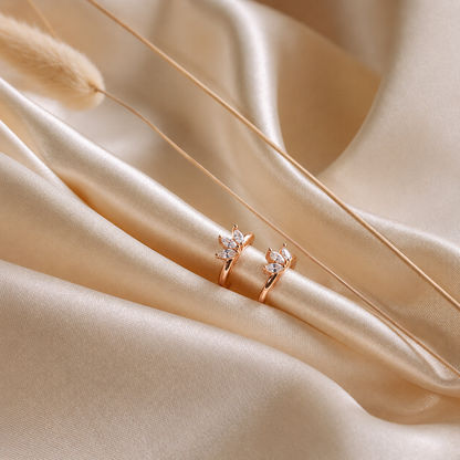 Two rose gold rings with clear gemstones, displayed on draped champagne-colored satin fabric.