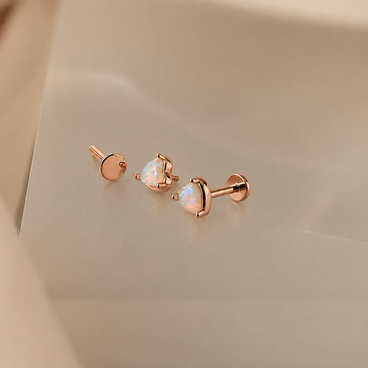 Rose gold earrings with heart-shaped gemstones on a beige background