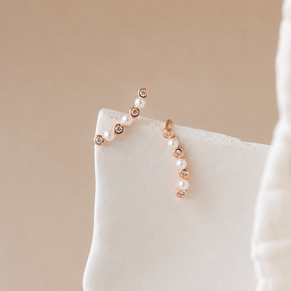 Pair of pearl earrings with rose gold accents on a white surface with a beige background