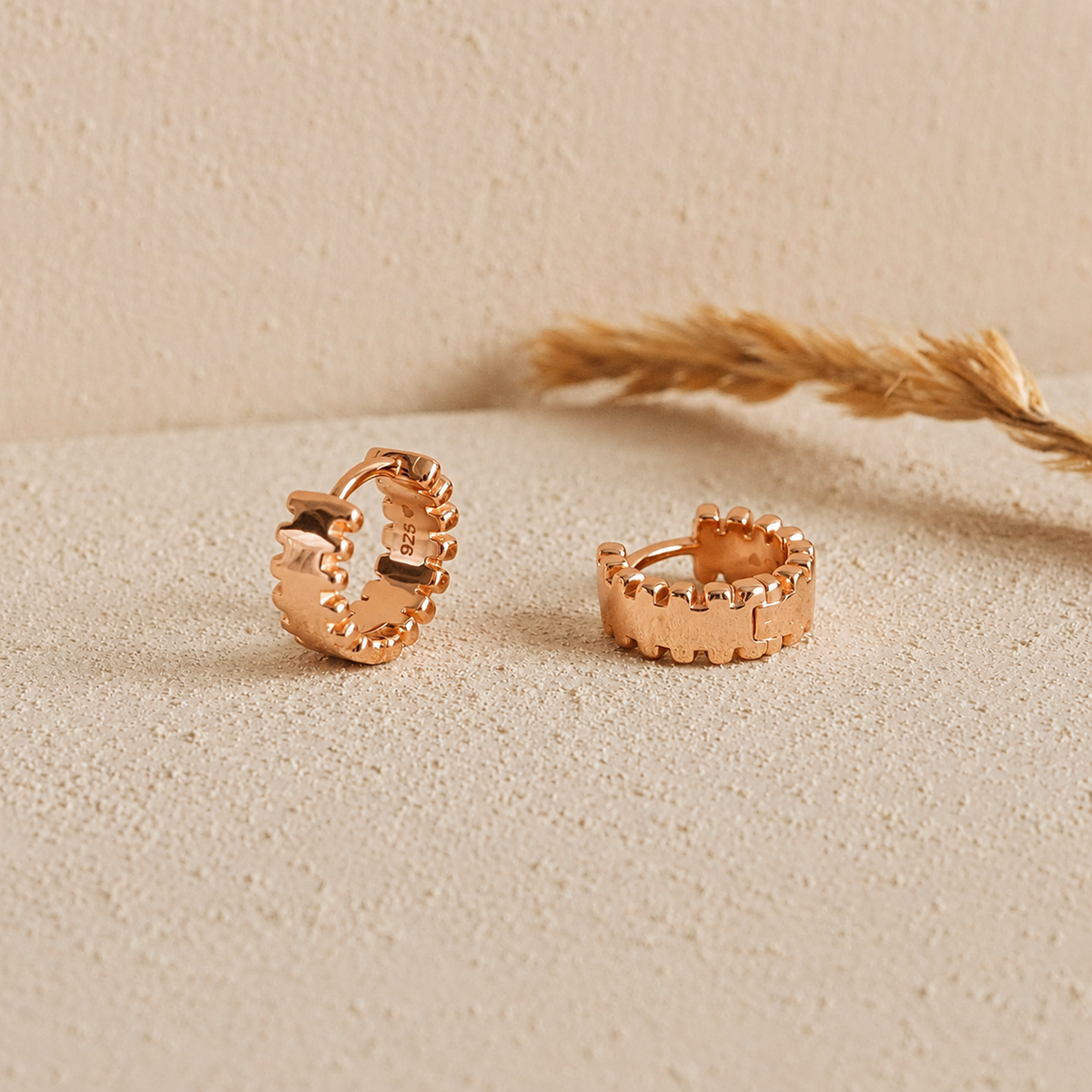 Rose gold hoop earrings on a beige surface with dried grass.