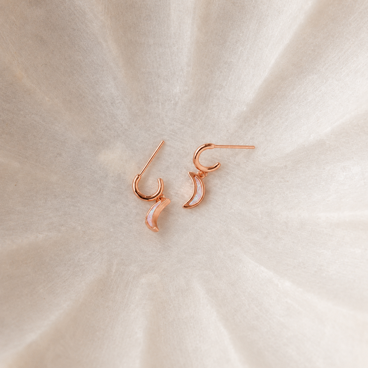 Rose gold earrings on a beige fabric background