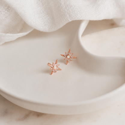 Rose gold star-shaped earrings on a white plate with a soft fabric background