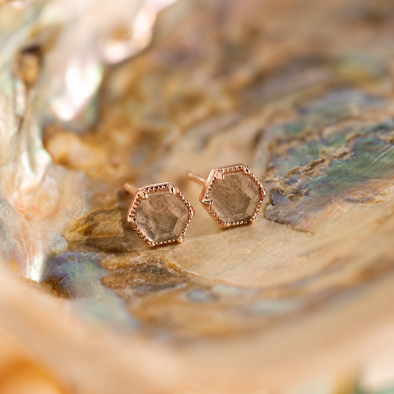 Hexagonal rose gold earrings on a textured surface