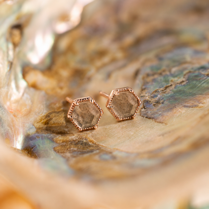 Hexagonal rose gold earrings on a textured surface