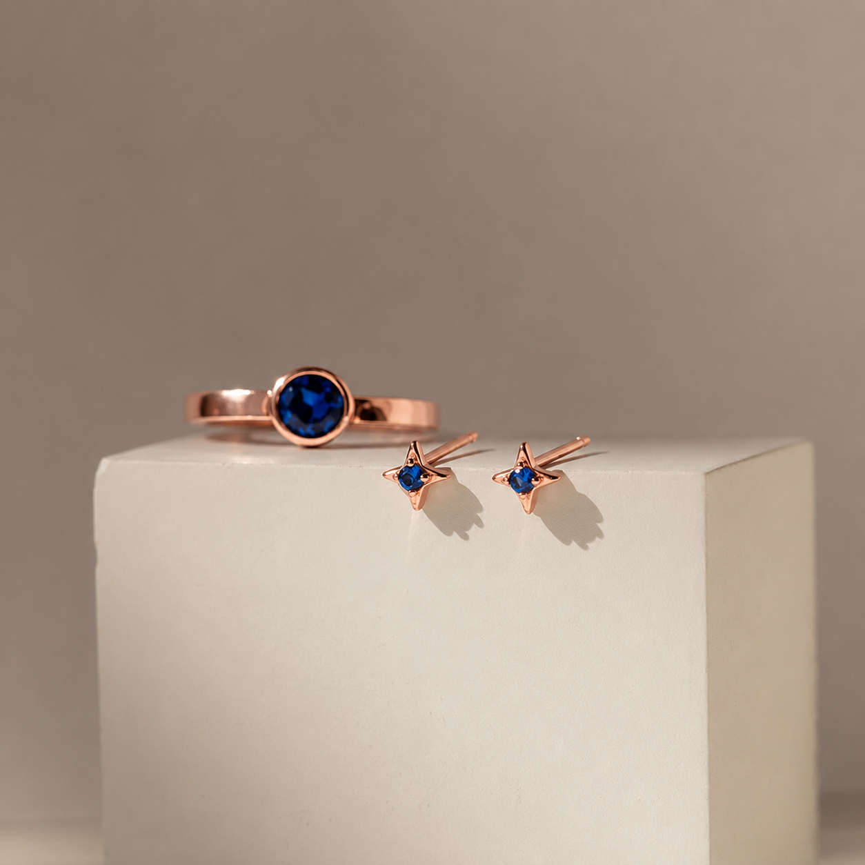 Rose gold ring and earrings with blue gemstones on a beige background