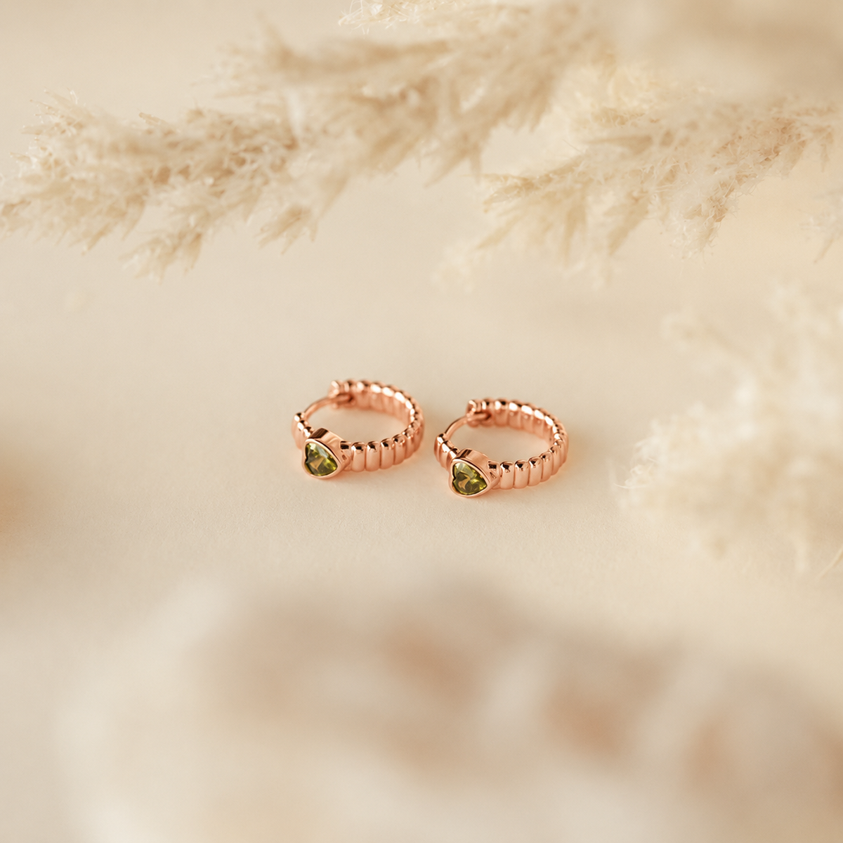 Rose gold hoop earrings with green gemstones on a soft beige background