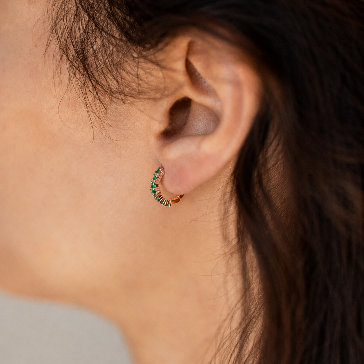Close-up of an ear wearing a colorful hoop earring with blurred background