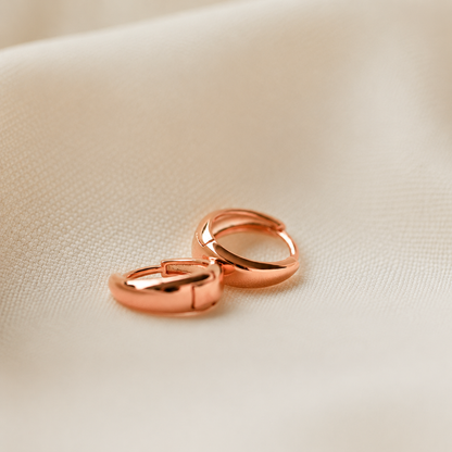 Rose gold hoop earrings on a beige fabric background
