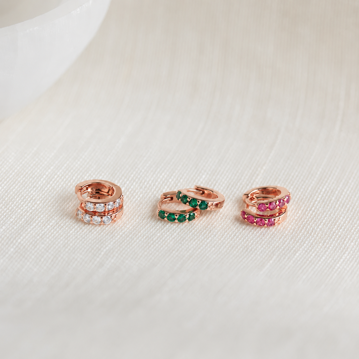 Three rose gold rings with gemstones on a light beige background