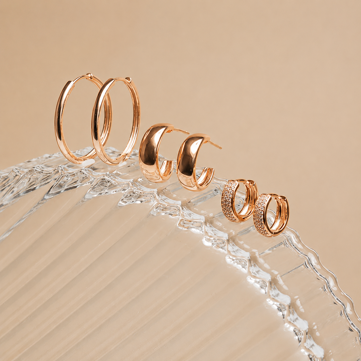 Set of gold hoop earrings on a decorative stand with a beige background
