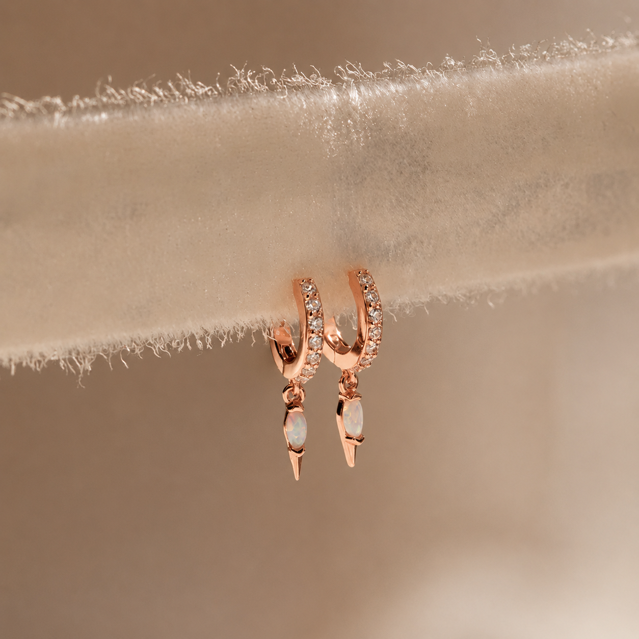 Rose gold hoop earrings with small stones on a beige fabric background