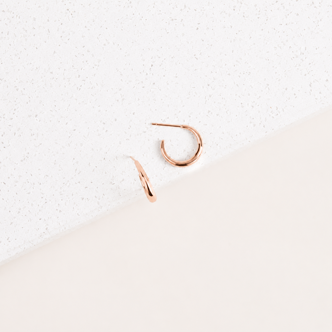 Rose gold hoop earrings on a textured white surface
