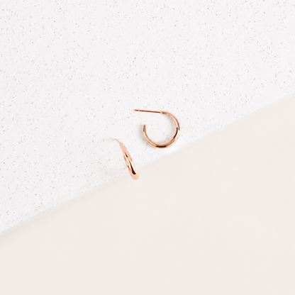 Rose gold hoop earrings on a textured white surface