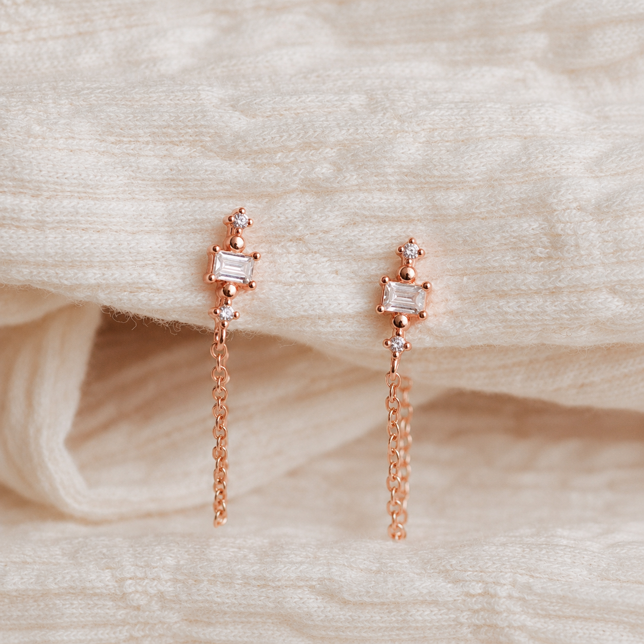 Rose gold earrings with chain drops on a soft beige fabric background