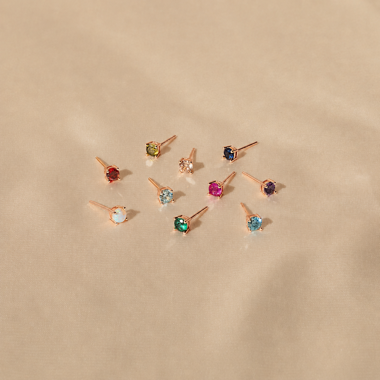 Set of small stud earrings with colored gemstones on a beige background