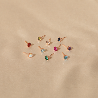 Set of small stud earrings with colored gemstones on a beige background