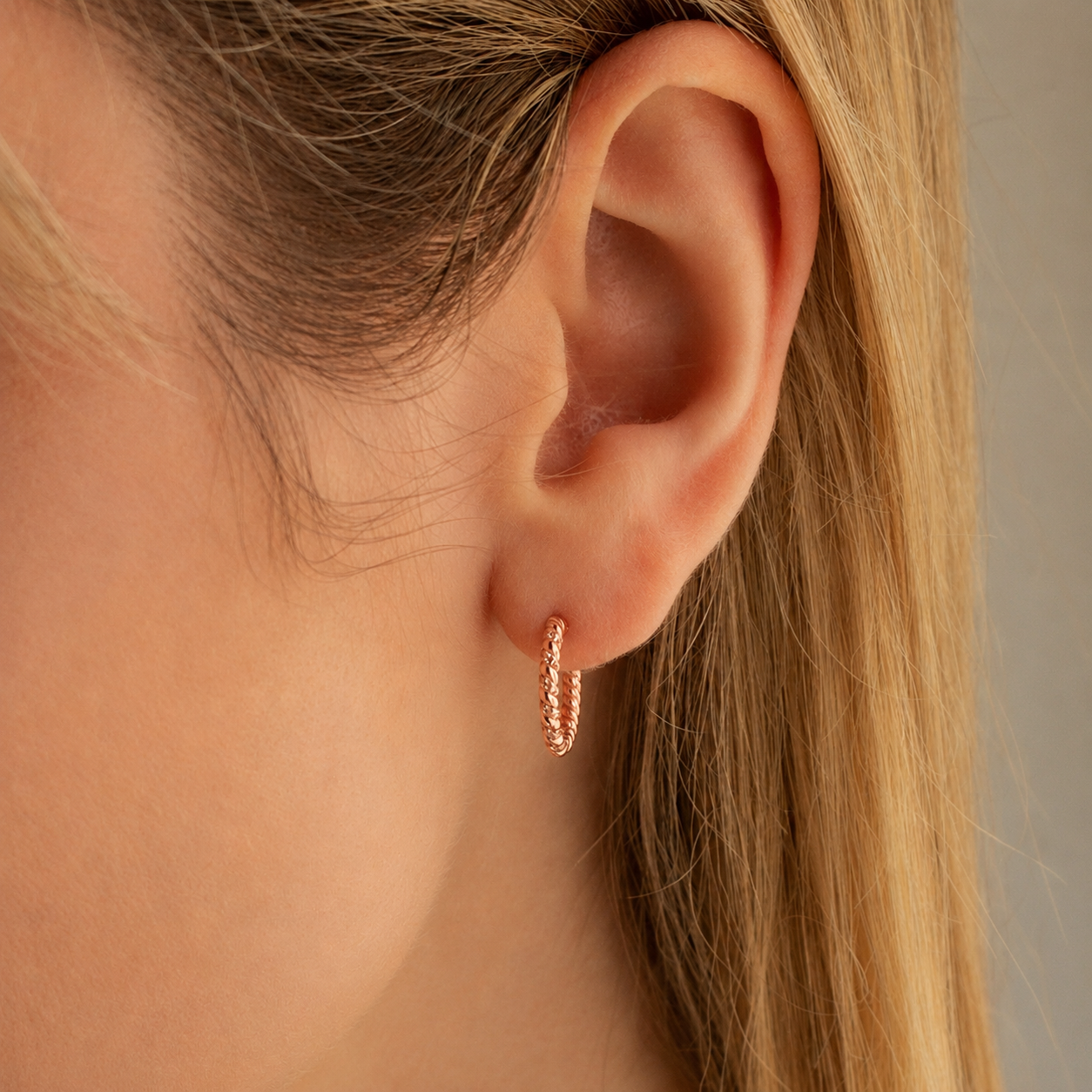 Close-up of an ear wearing a rose gold hoop earring with a neutral background
