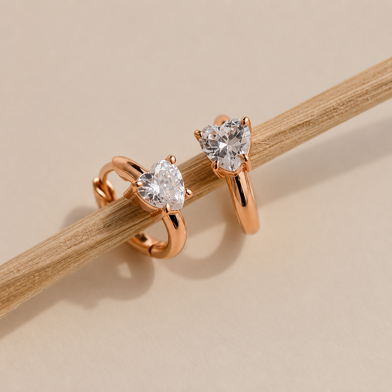 Rose gold heart-shaped diamond earrings on a wooden stick against a beige background