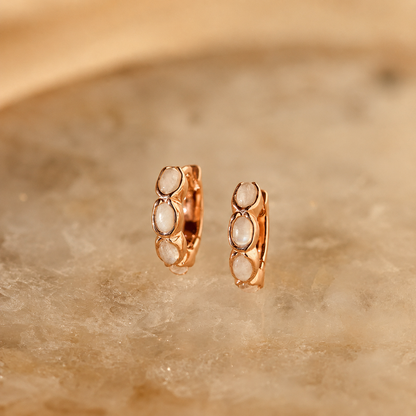 Rose gold hoop earrings with embedded stones on a beige stone background