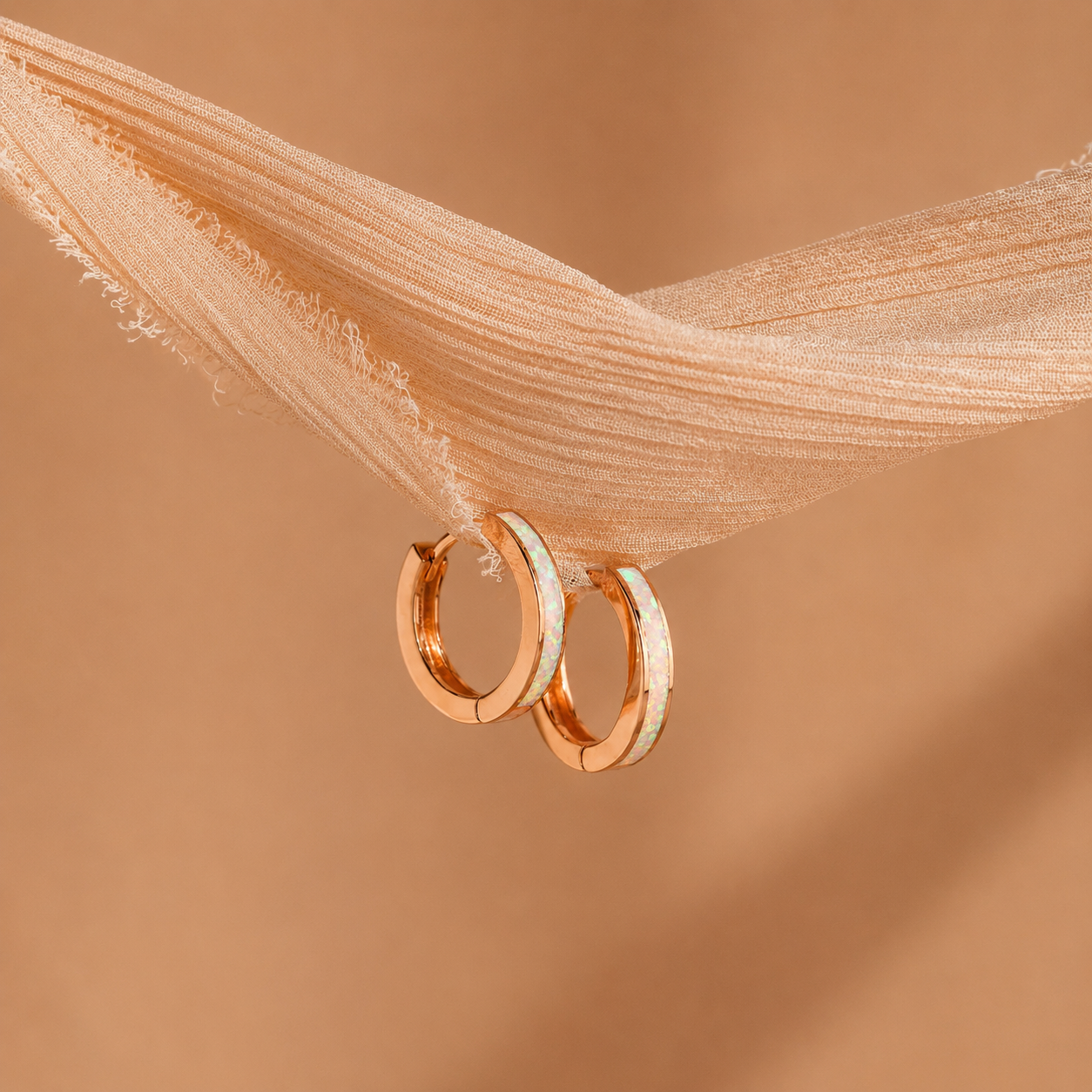 Rose gold hoop earrings on a soft brown fabric background