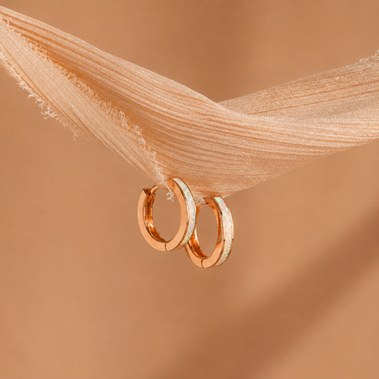 Rose gold hoop earrings on a soft brown fabric background